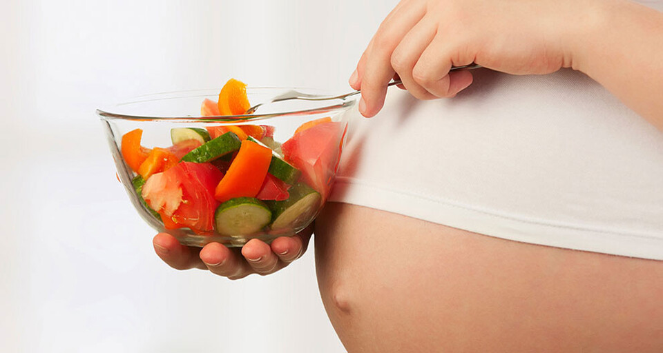 A pregnant woman eating bowl a healthy mix of fruits and vegetables on a bowl.