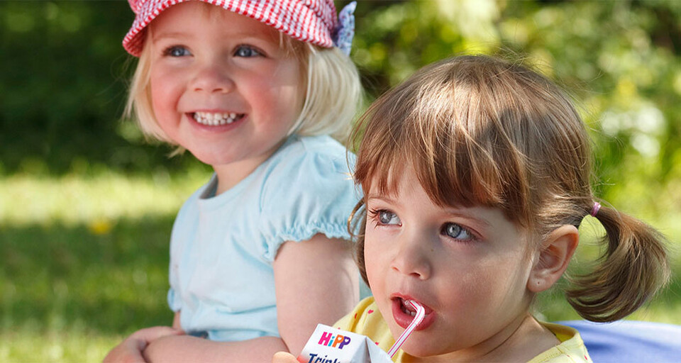 Two young girls outdoors with one of them drinking a HIPP milk product.