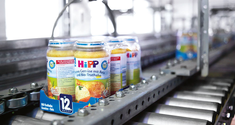 HiPP jar products wrapped together by sustainalbe plastic packaging on a supply belt inside a production factory.