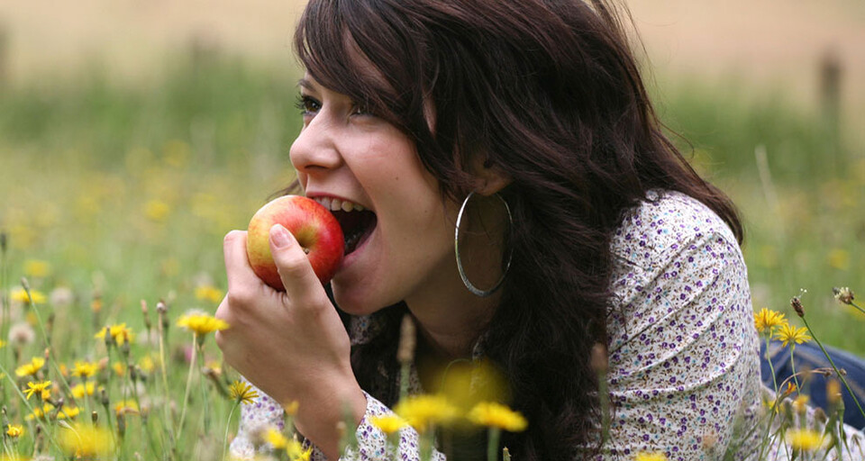 A woman taking a bite of an apple while laying on her stomach on a field.