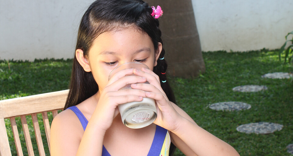 A young girl drinking a glass of HIPP milk.