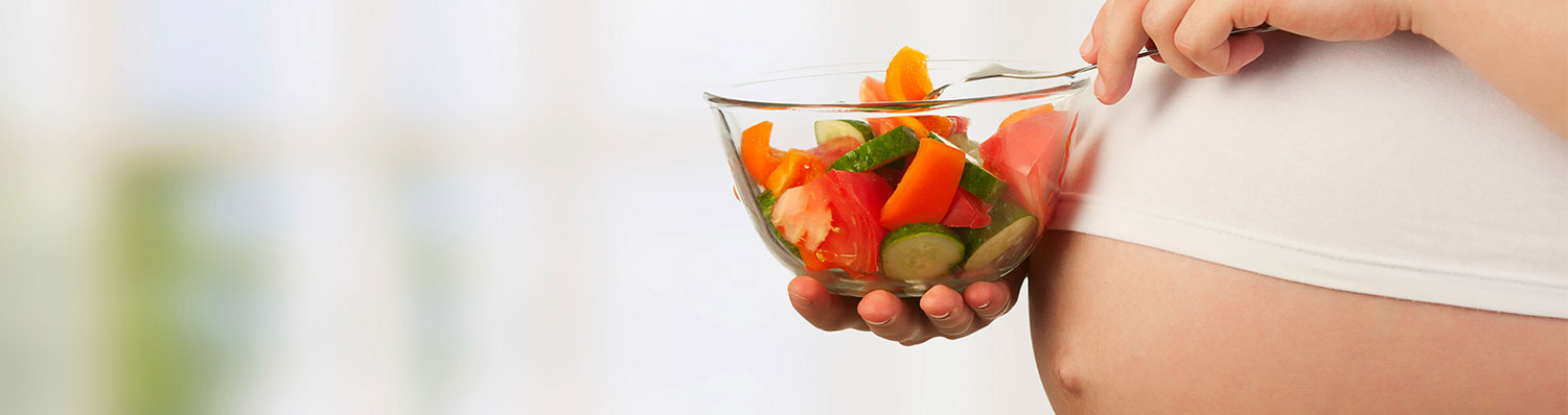 A pregnant woman eating bowl a healthy mix of fruits and vegetables on a bowl.